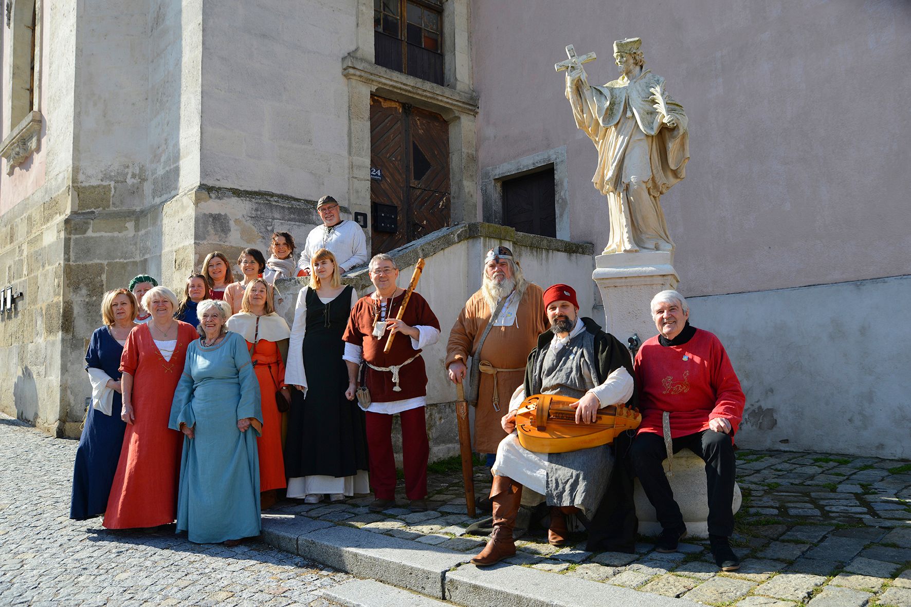 Gruppe von Menschen in mittelalterlicher Kleidung vor einer Statue in einer Altstadt.