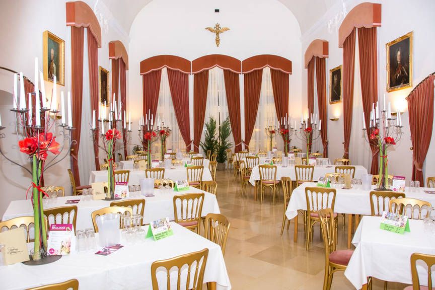 Eleganter Saal mit gedeckten Tischen, Kerzenleuchtern und roten Vorhängen.