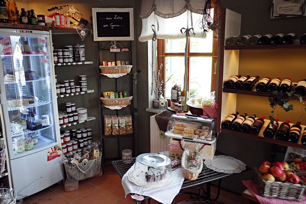 Innenansicht eines Bauernladens mit Regalen voller Weinflaschen, Marmeladen und Gebäck.