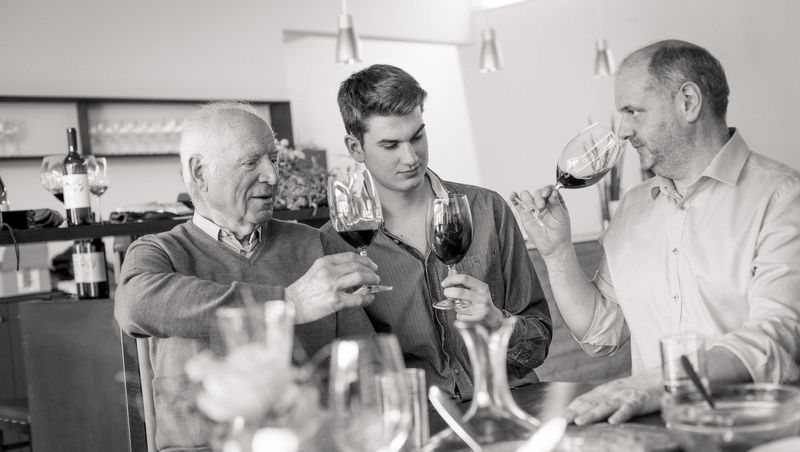 Drei Männer stoßen mit Weingläsern an einem Tisch an.