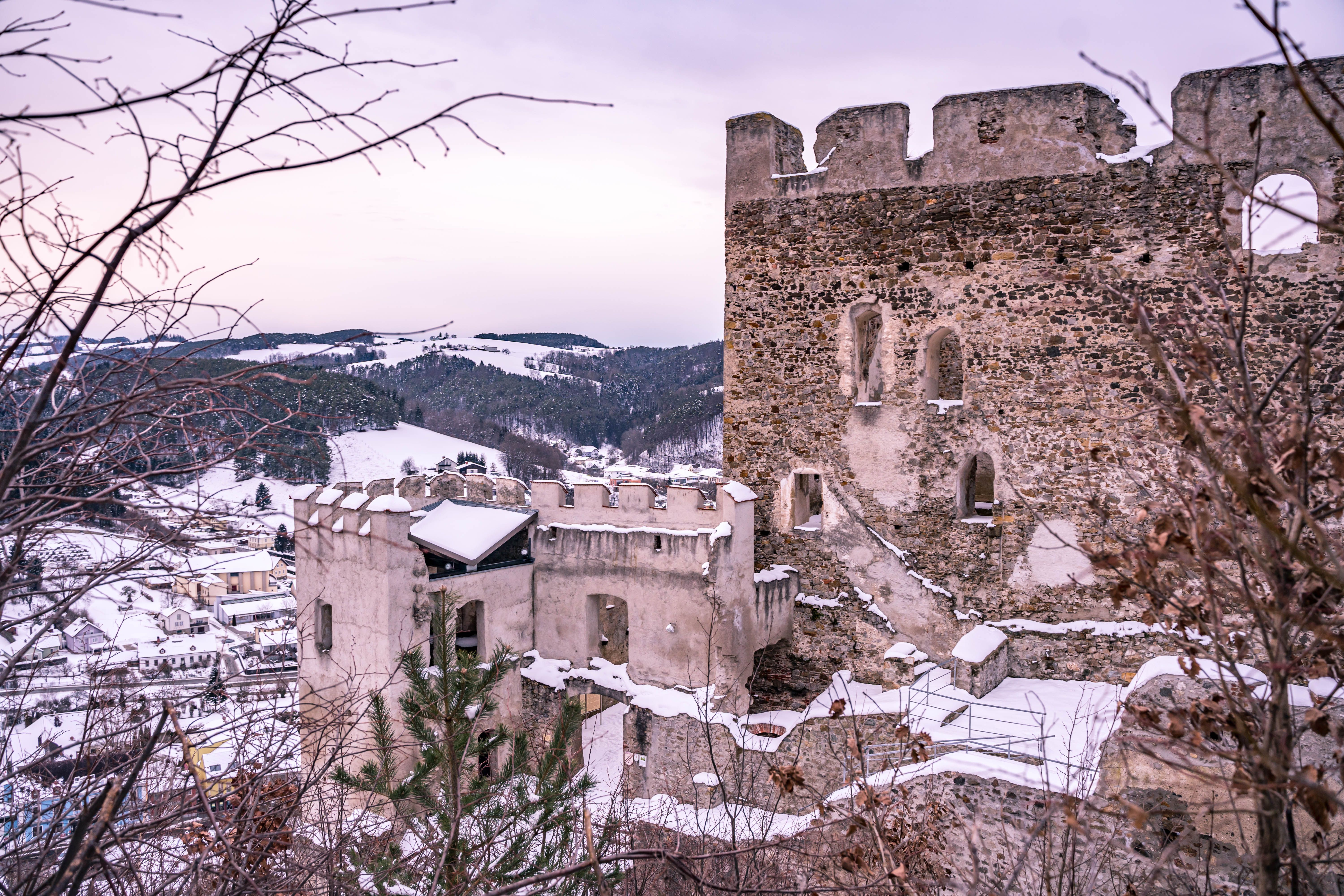 Winterliche Burgruine Kirchschlag in Österreich mit schneebedeckten Mauern und Hügeln im Hintergrund.