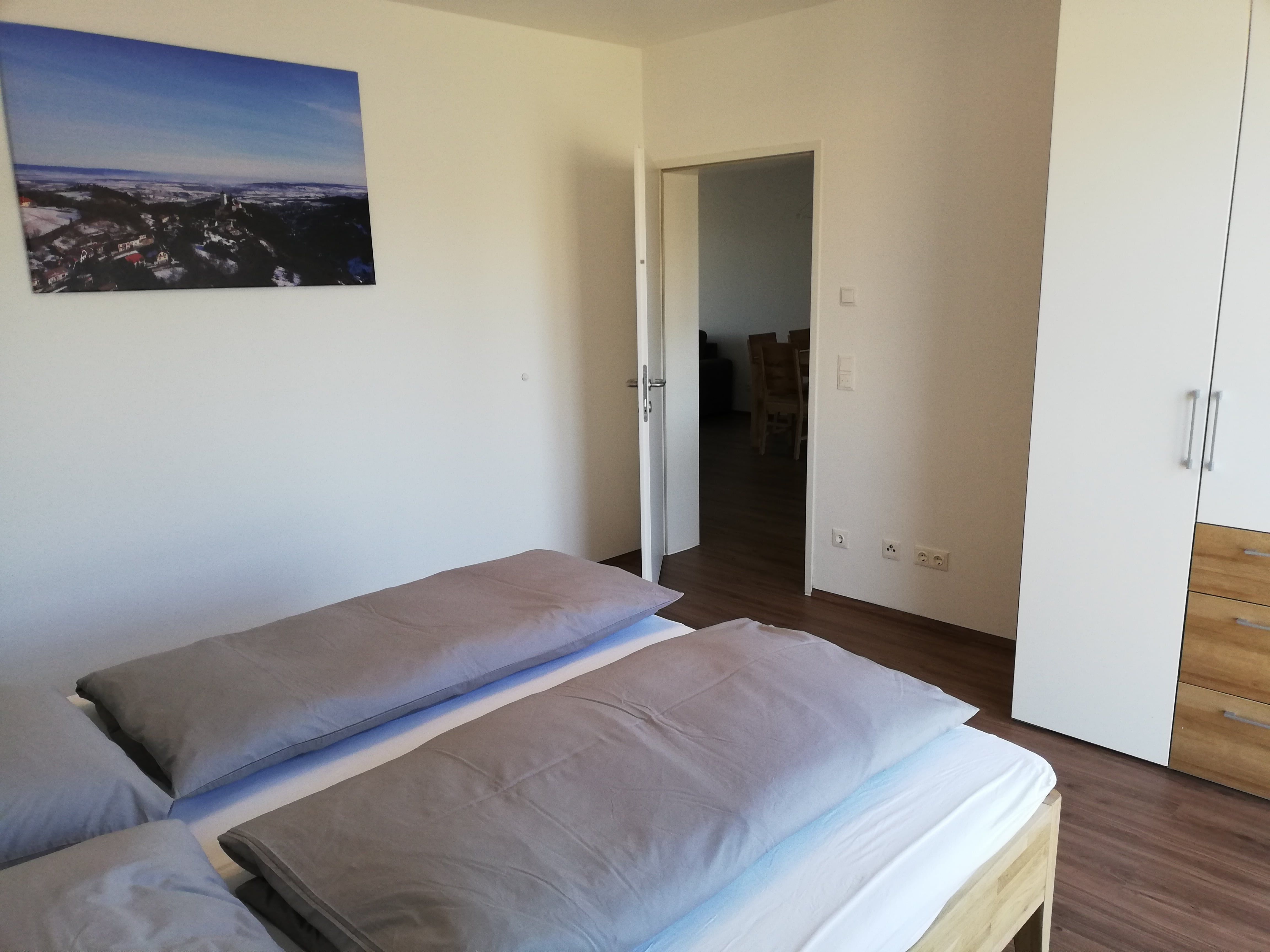 Modernes Schlafzimmer mit Doppelbett, weißem Kleiderschrank und Landschaftsbild an der Wand.