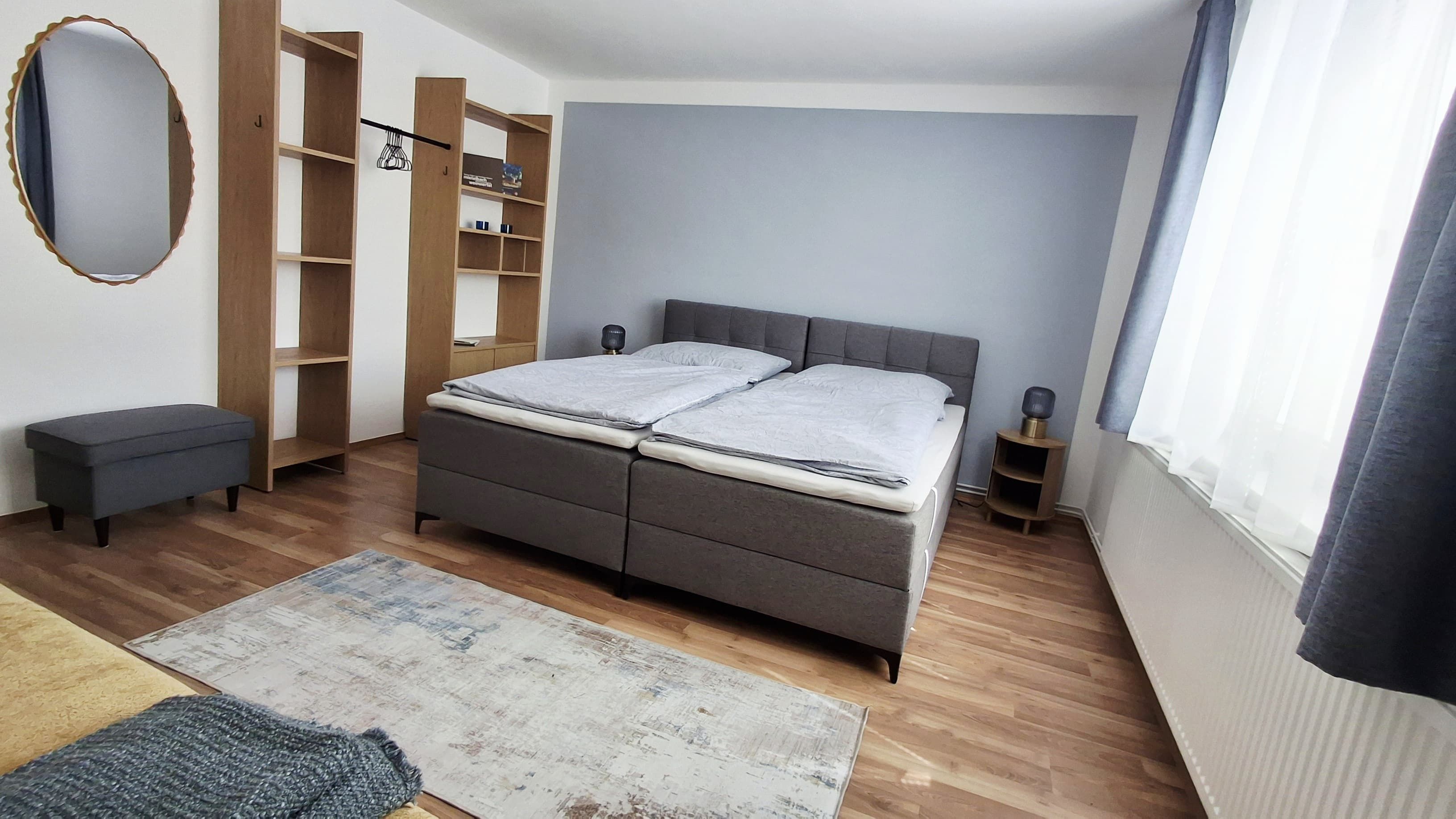 Modern eingerichtetes Gästezimmer mit Doppelbett, grauen Vorhängen und Holzmöbeln.