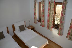 Zwei Einzelbetten in einem hellen Gästezimmer mit Blumenmustervorhängen.