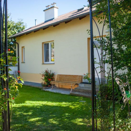 Ein gelbes Haus mit Gartenbank und Blumen im Vordergrund.