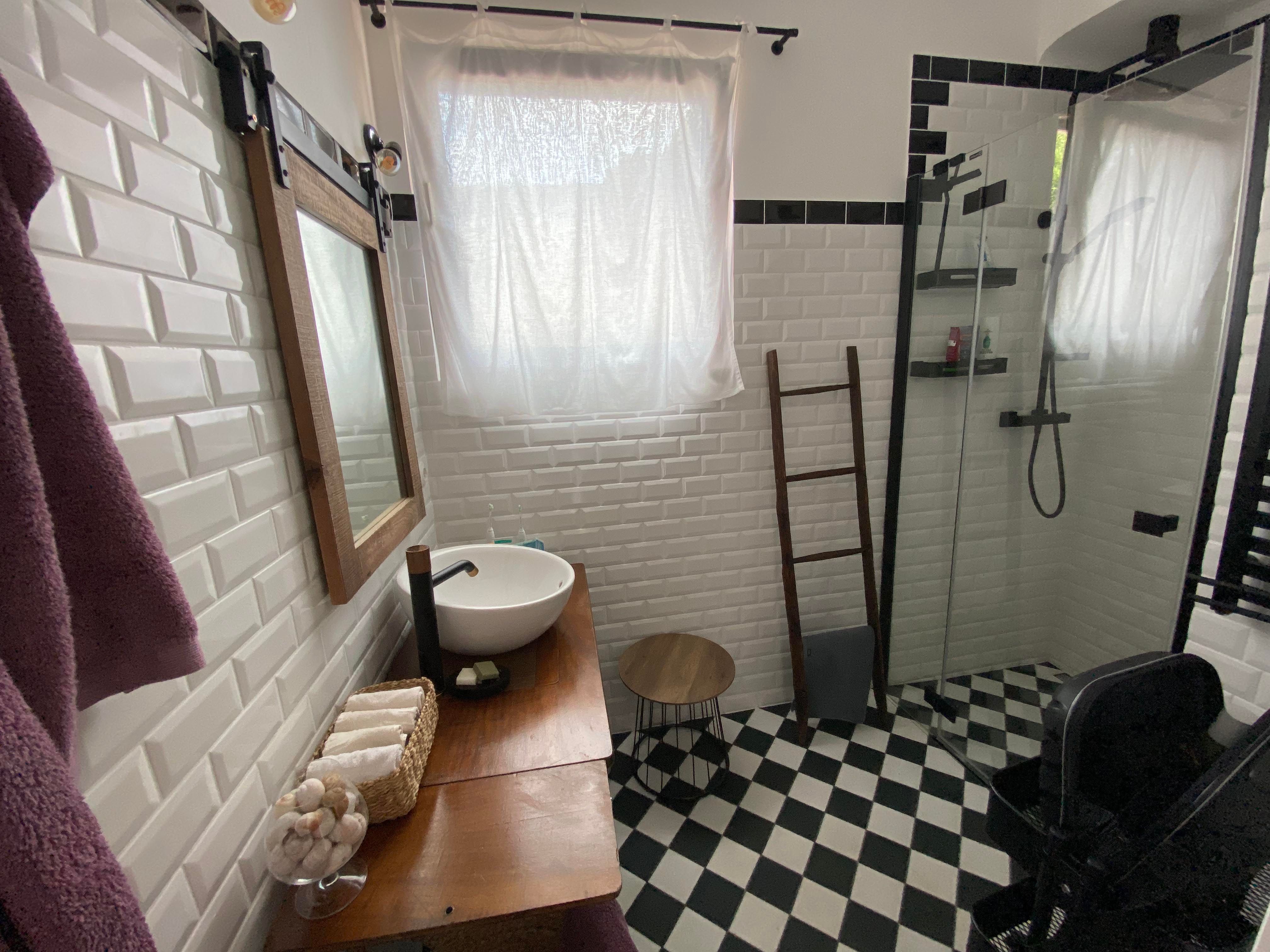 Modernes Badezimmer mit weiß gefliesten Wänden, schwarzem und weißem Schachbrettboden, Waschbecken, Spiegel und Dusche.
