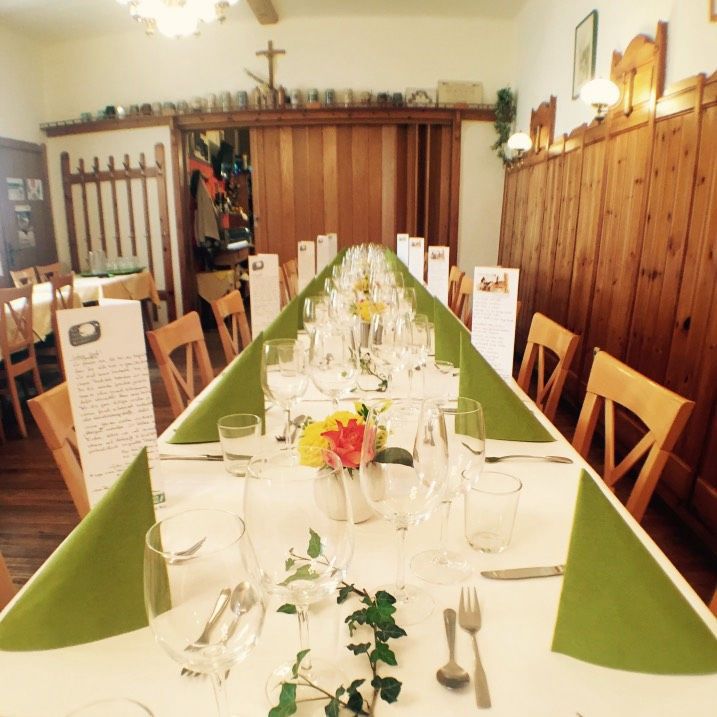 Langer, festlich gedeckter Tisch in einer rustikalen Gaststube mit Holzwänden und Dekoration.