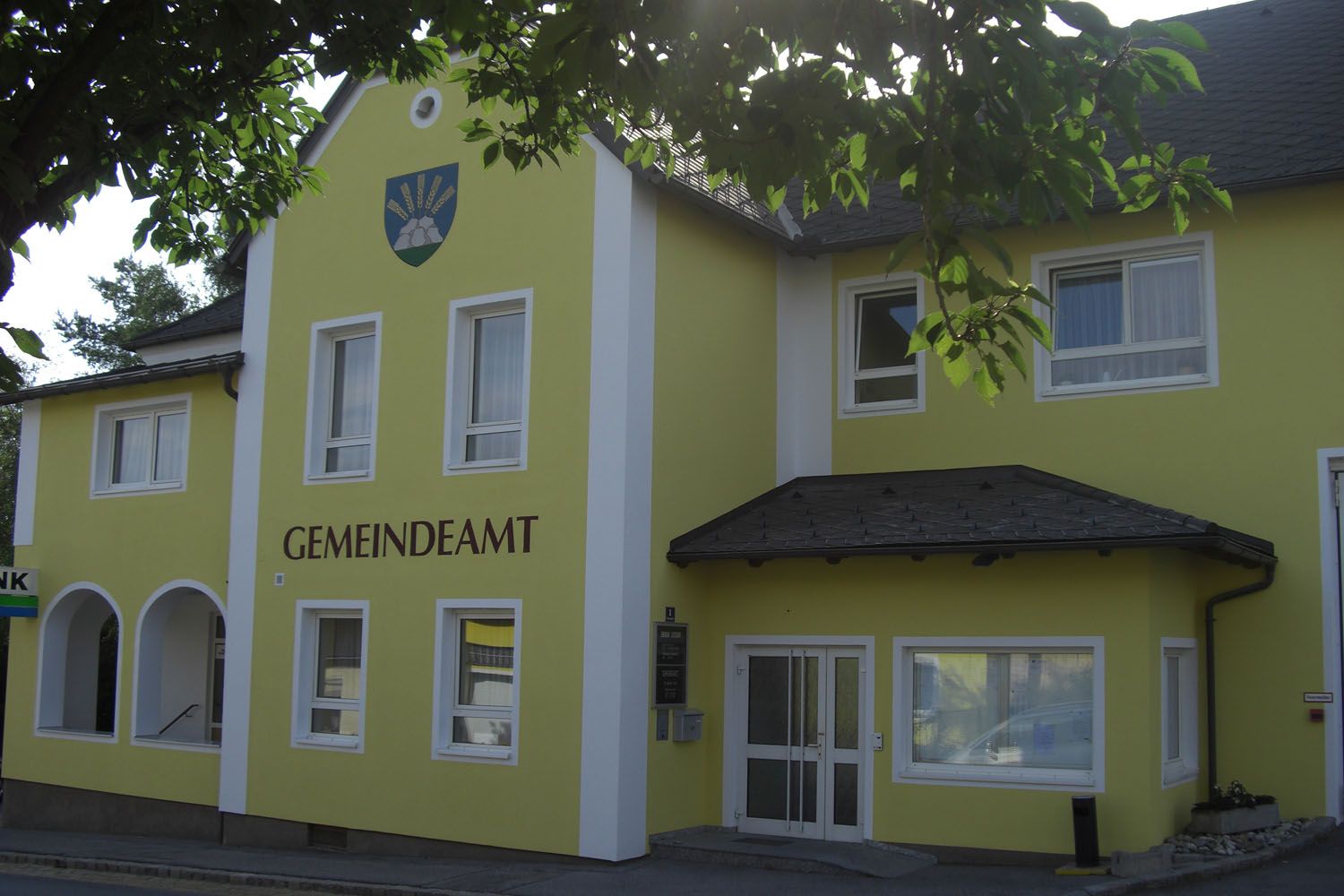 Gelbes Gebäude mit der Aufschrift 'GEMEINDEAMT' und einem Wappen darüber.