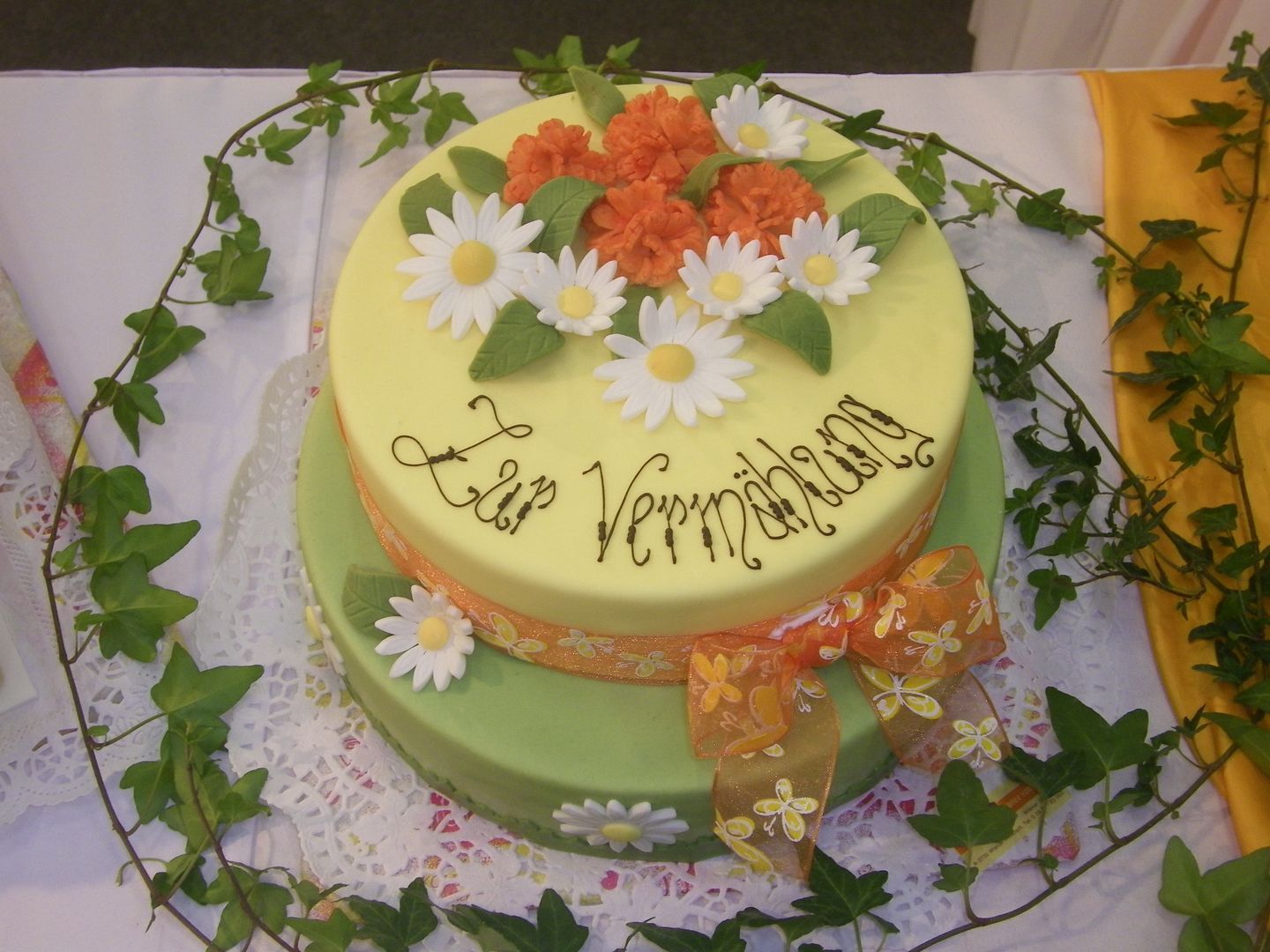 Zweistöckige Torte mit Blumen und Schriftzug 'Zur Vermählung'.