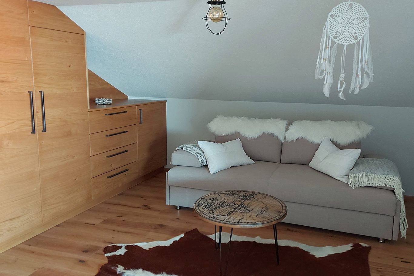Gemütliches Zimmer mit Ausziehcouch, Holzmöbeln und Traumfänger.