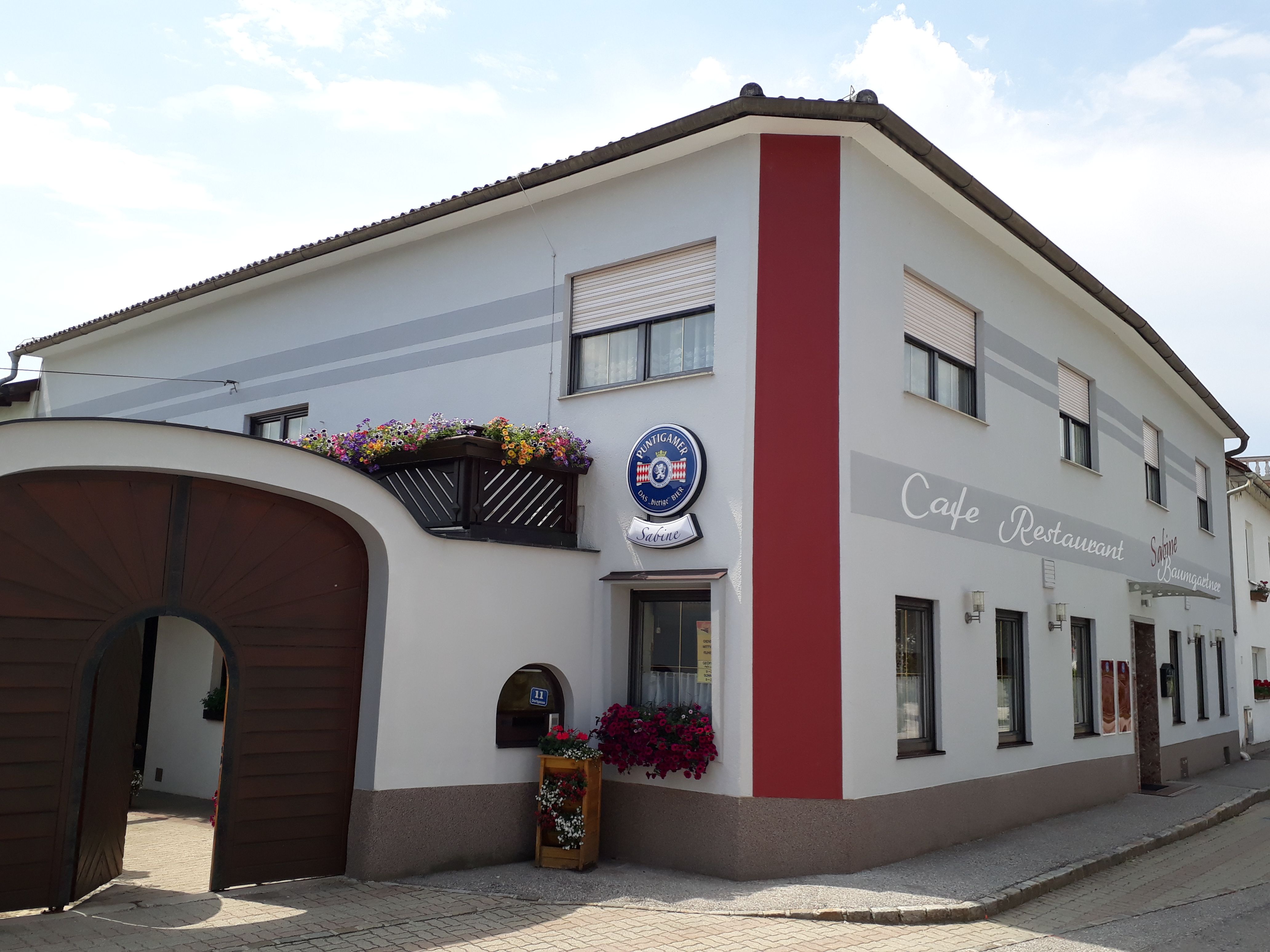 Außenansicht Café Sabine mit Holztor, weiß-roter Fassade und Aufschrift "Café-Restaurant".
