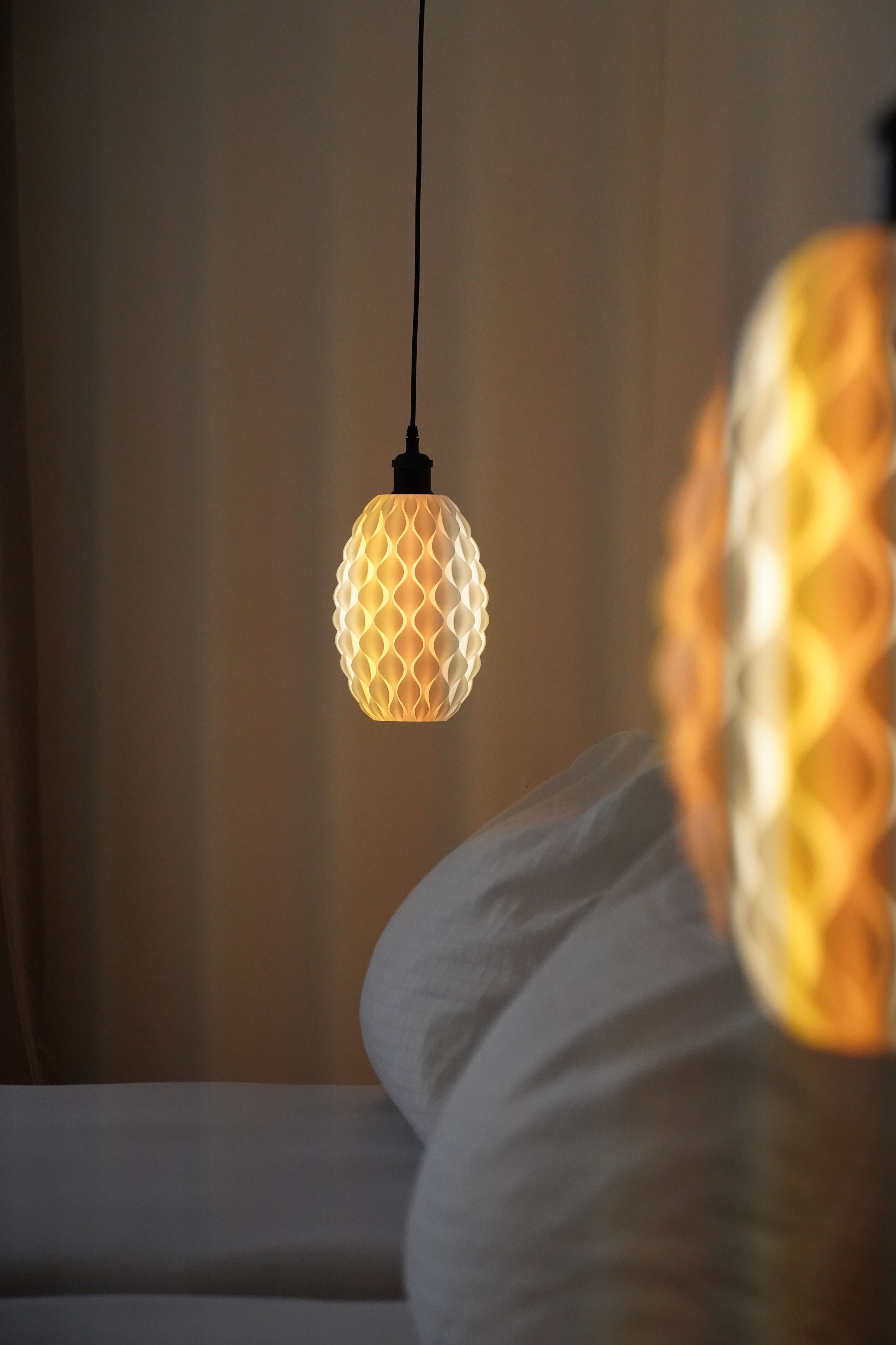 Nahaufnahme einer hängenden Lampe mit wabenartigem Muster, die warmes Licht ausstrahlt, neben einem Bett.