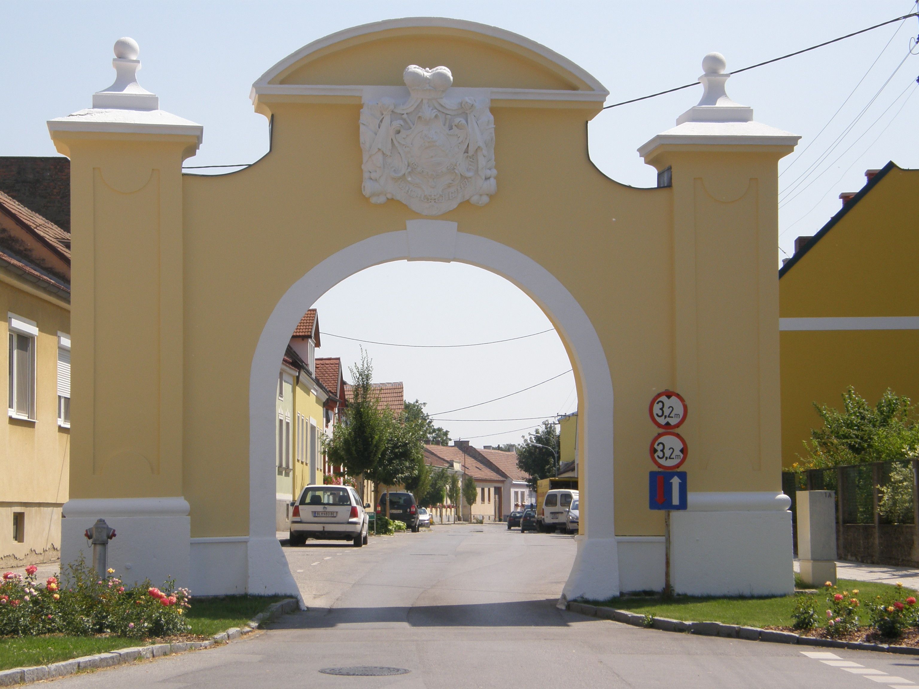 Gelbes Tor mit Wappen, das eine Straße überspannt.