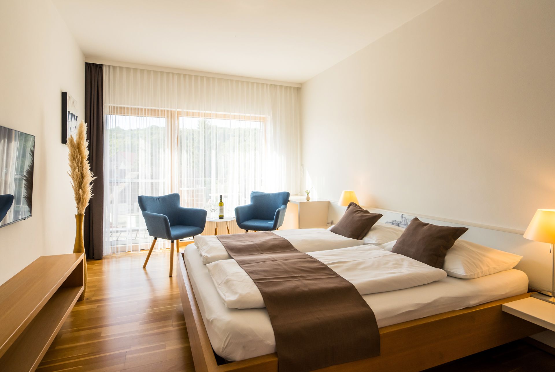 Modernes Gästezimmer mit Doppelbett, blauen Sesseln und großen Fenstern.