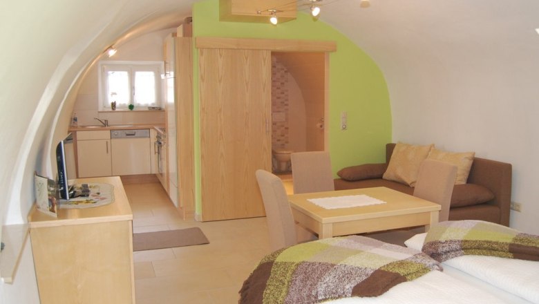 Gem&uuml;tliches Apartment mit gew&ouml;lbter Decke, K&uuml;che, Esstisch, Sofa und Bett.