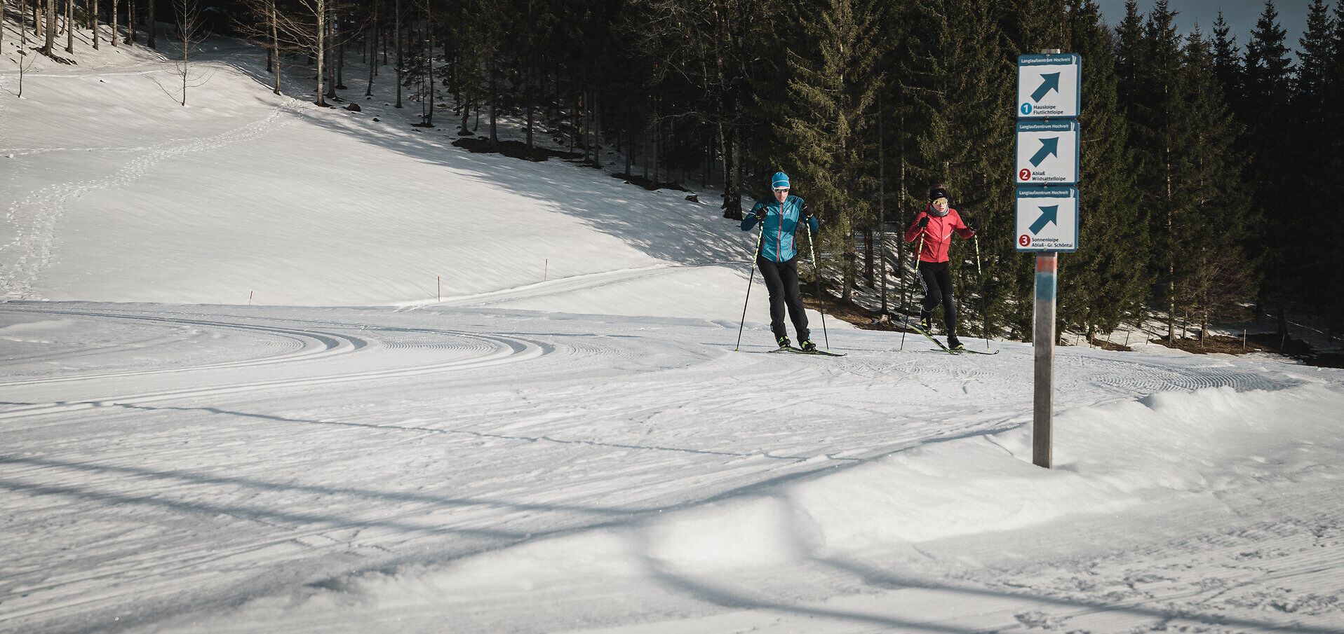 Die glitzernde Schneedecke erstreckt sich über die sanften Hügel der Ybbstaler Alpen, während zwei Langläufer in lebhaften Farben die ruhige Winterlandschaft durchqueren. Die frische, klare Luft und die majestätischen Tannen schaffen eine perfekte Kulisse für ein unvergessliches Winterabenteuer.