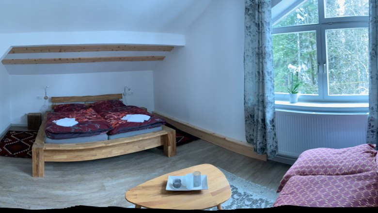 Gemütliches Schlafzimmer mit Holzbett, Sofa und großem Fenster mit Vorhängen.