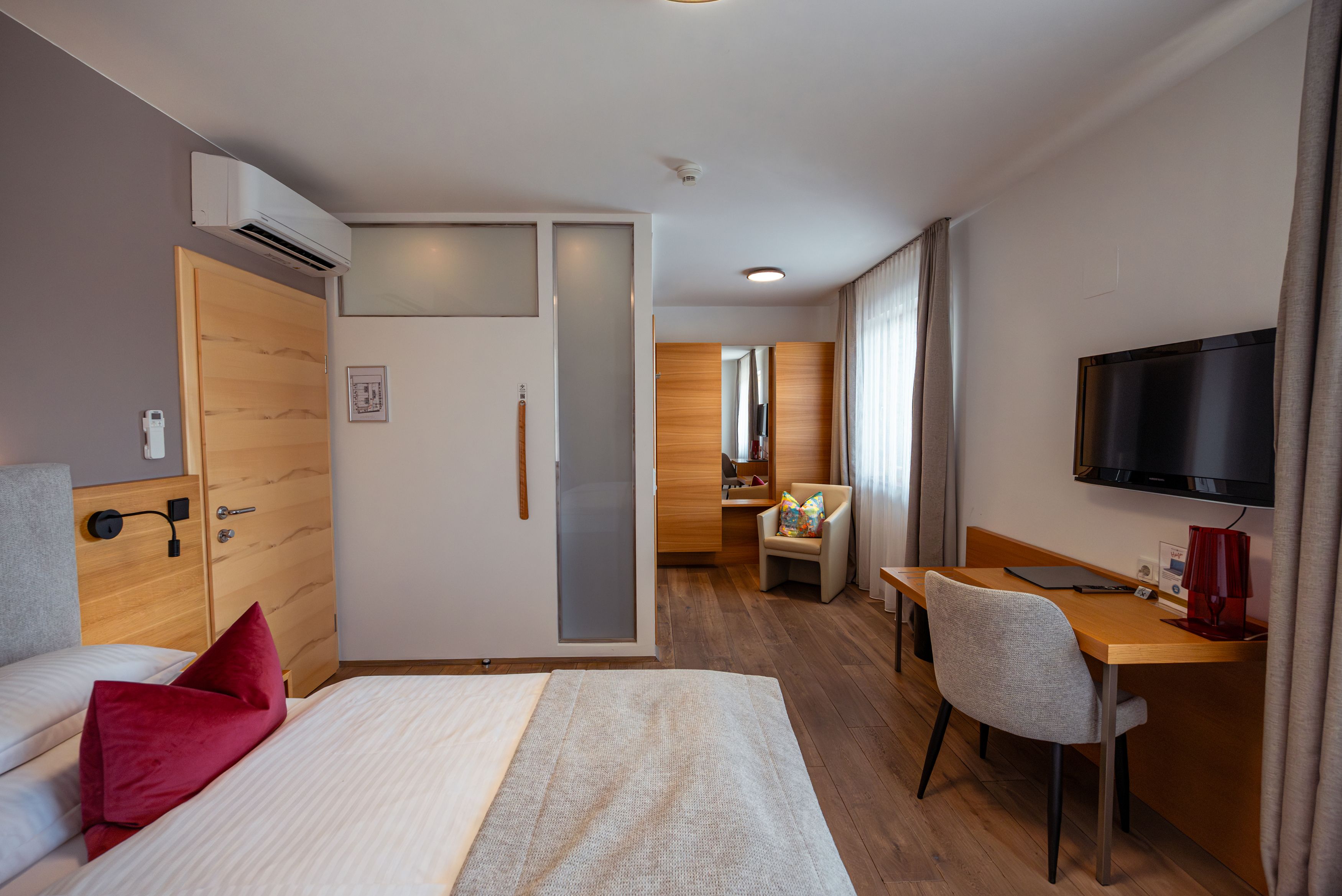 Modern eingerichtetes Hotelzimmer mit Bett, Schreibtisch, Stuhl und Fernseher.