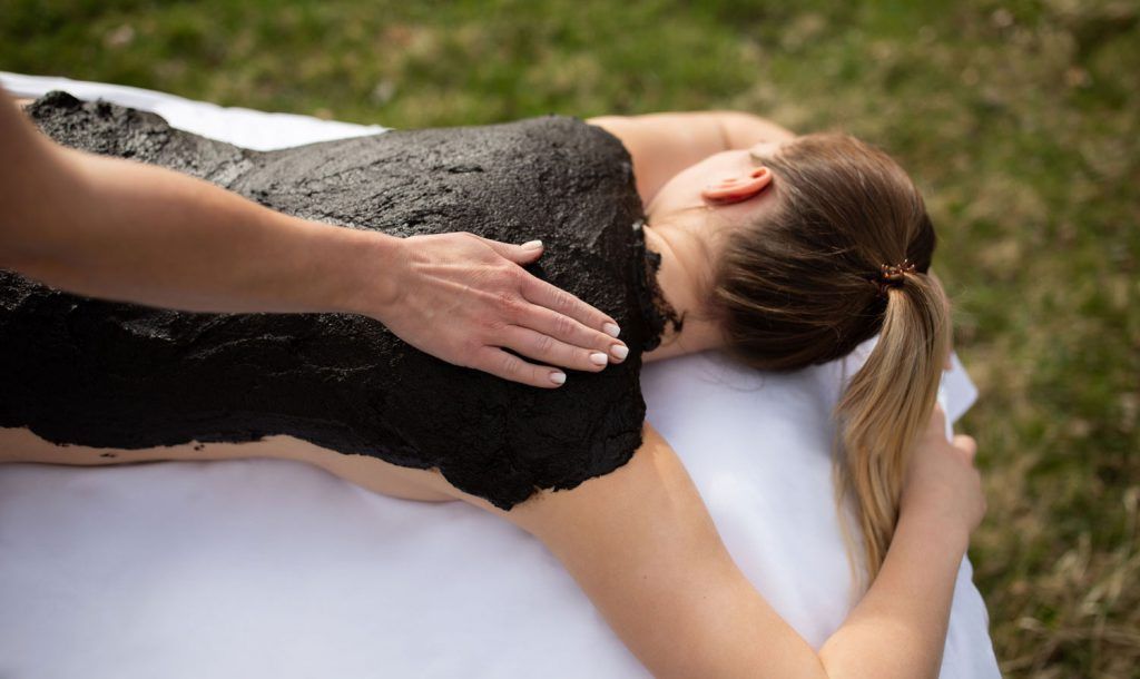 Person erhält eine Moorpackung auf dem Rücken im Freien.