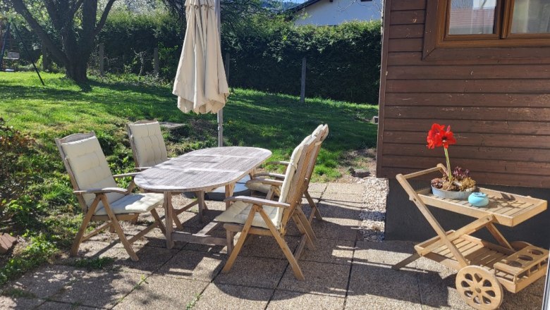 Terrasse mit Holzmöbeln und Sonnenschirm, umgeben von Garten.