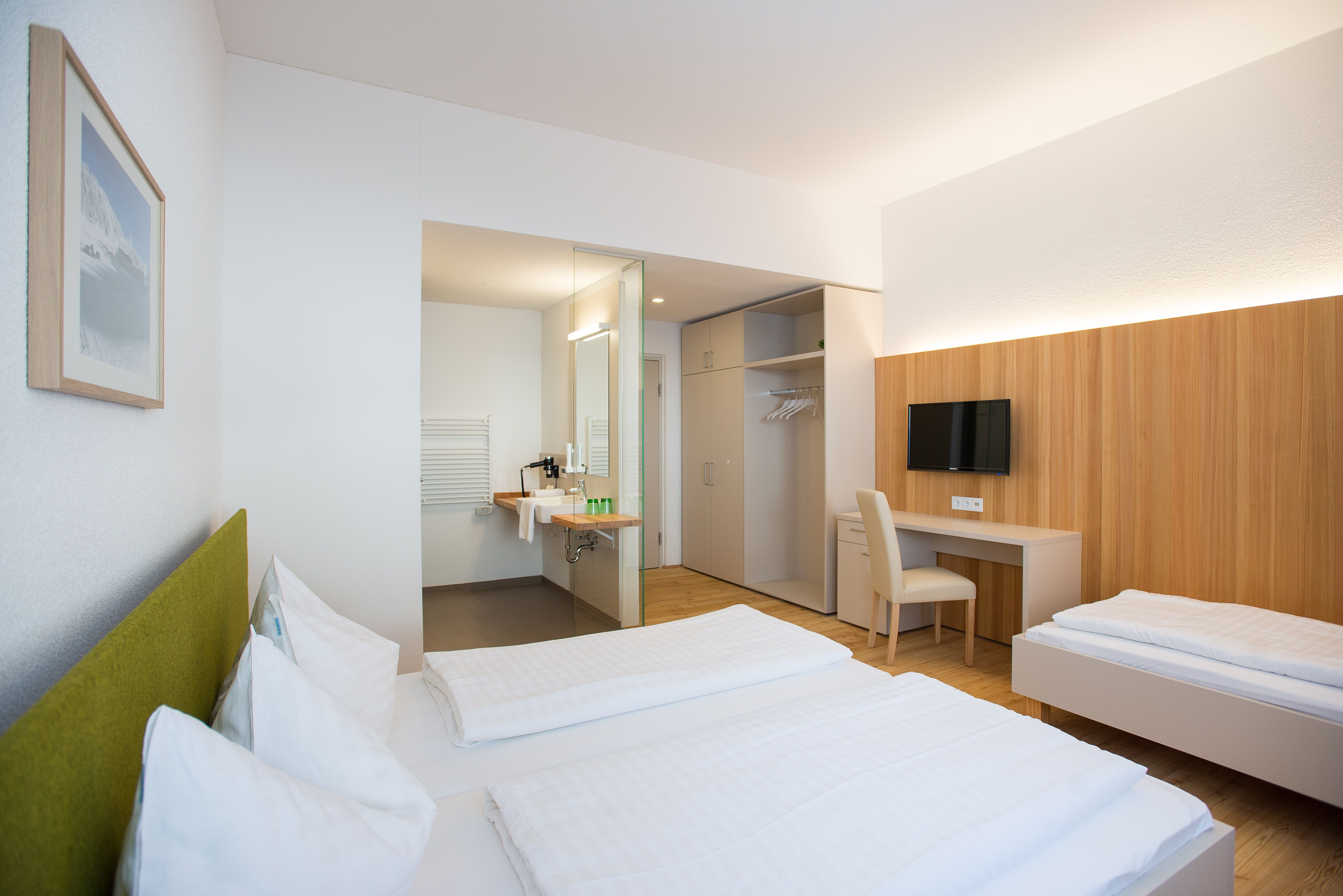 Modern eingerichtetes Hotelzimmer mit zwei Betten, Schreibtisch, Fernseher und offenem Badezimmer.