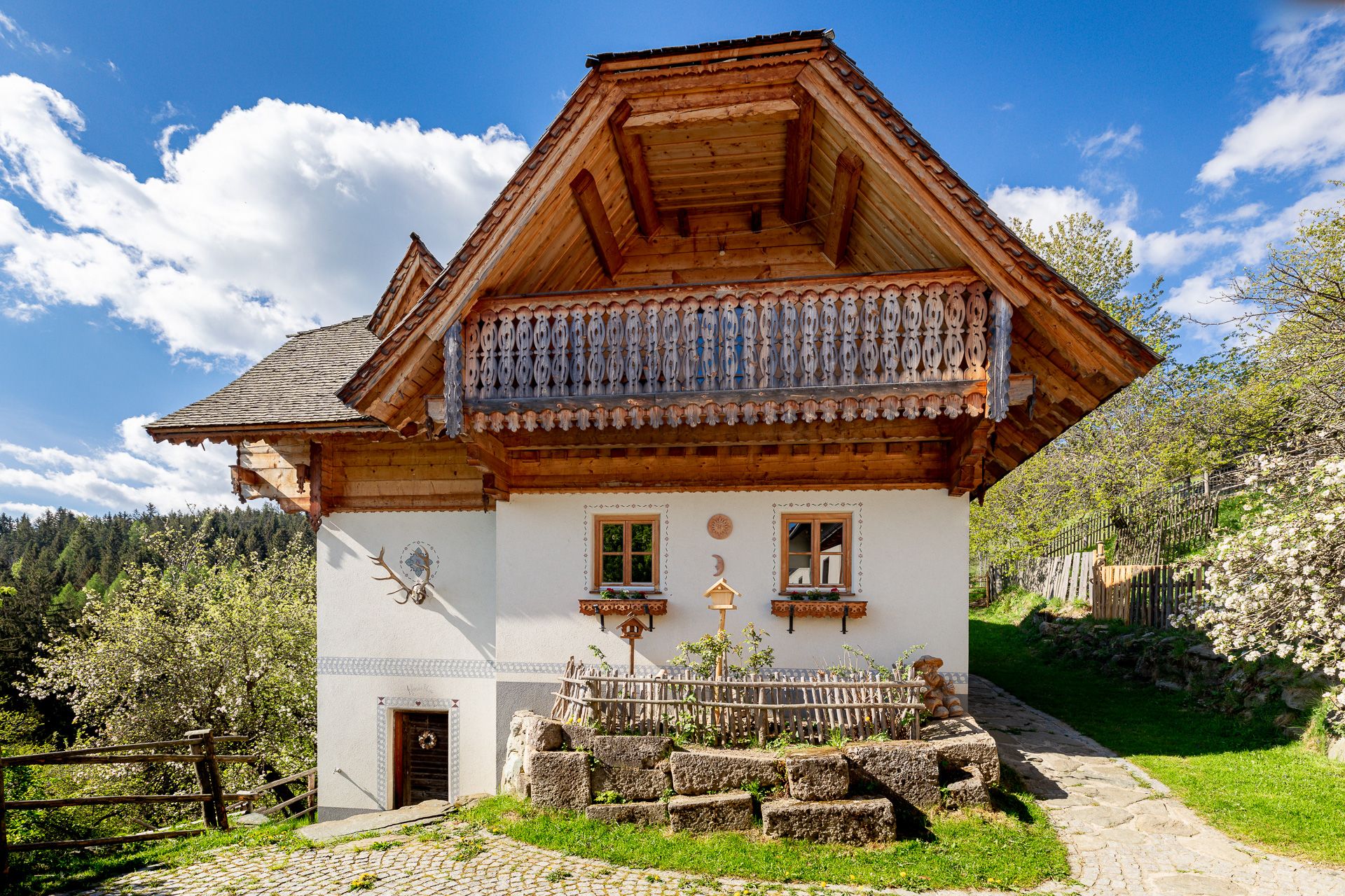 Traditionelles Haus mit Holzbalkon und weißer Fassade, umgeben von Natur.