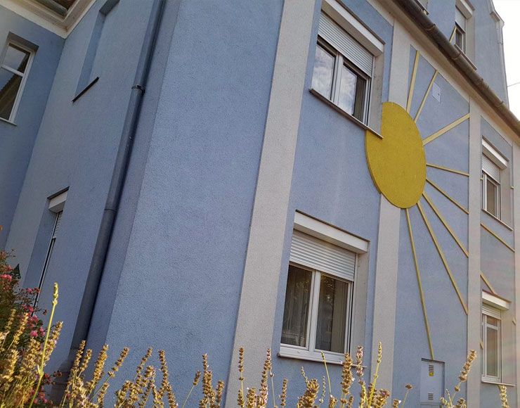 Blaues Haus mit gelber Sonnendekoration an der Fassade.