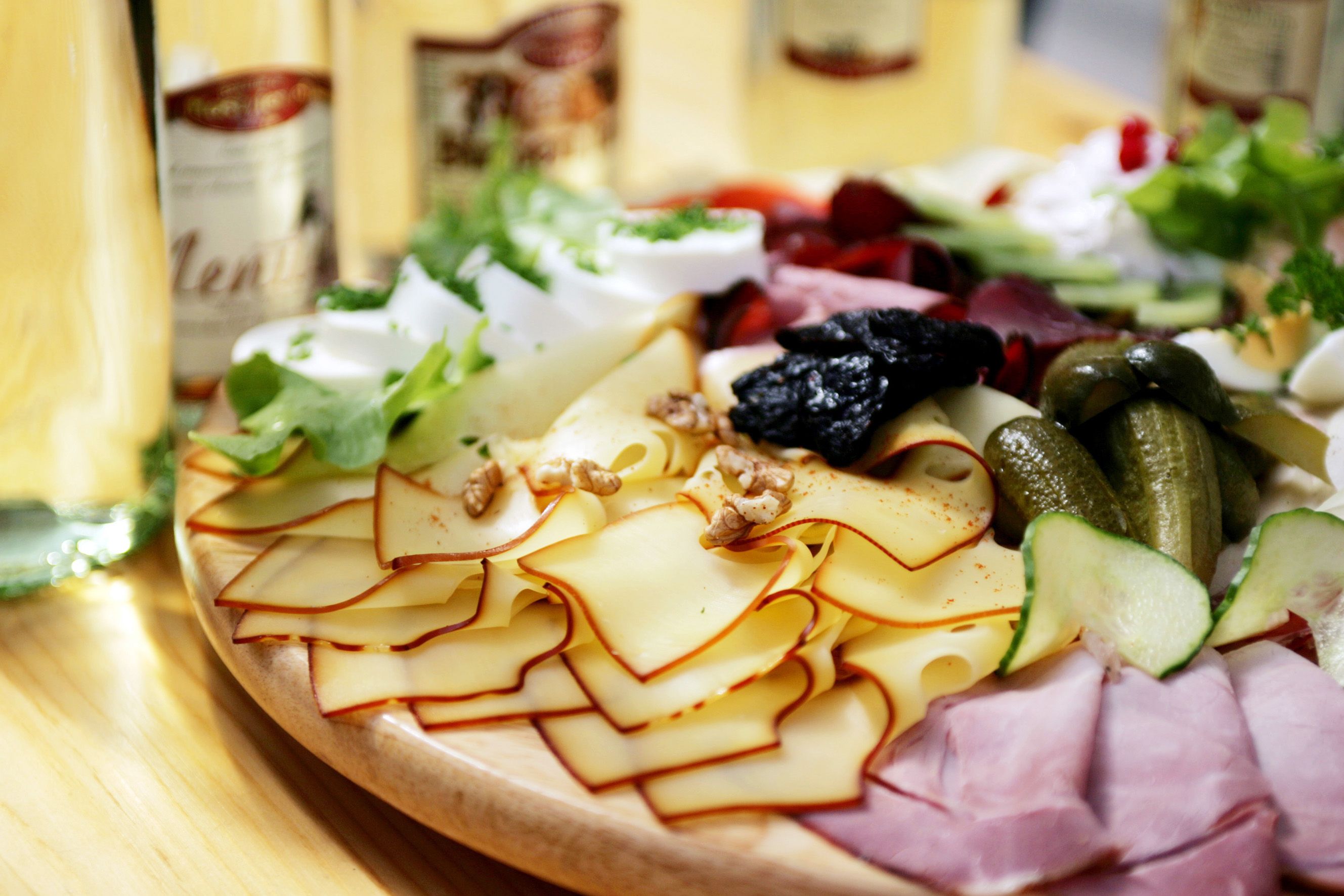 Ein Jausenbrett mit Käse, Schinken, Gurken, Nüssen und Salat auf einem Holztisch.