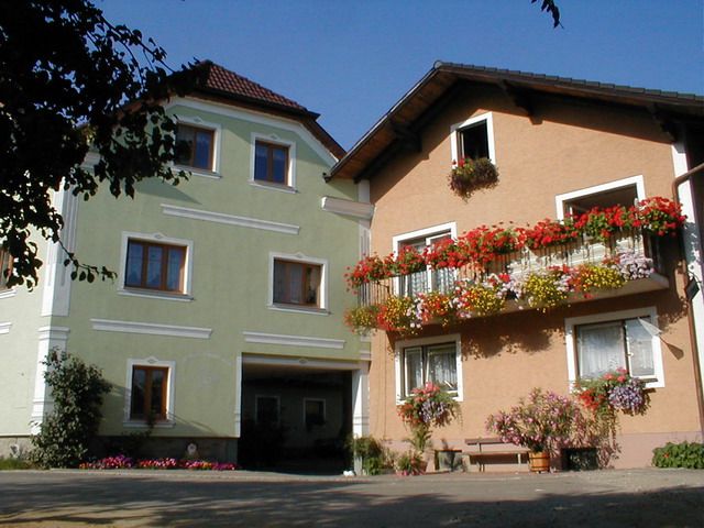 Zwei Bauernhofgebäude mit bunten Blumen an den Balkonen.