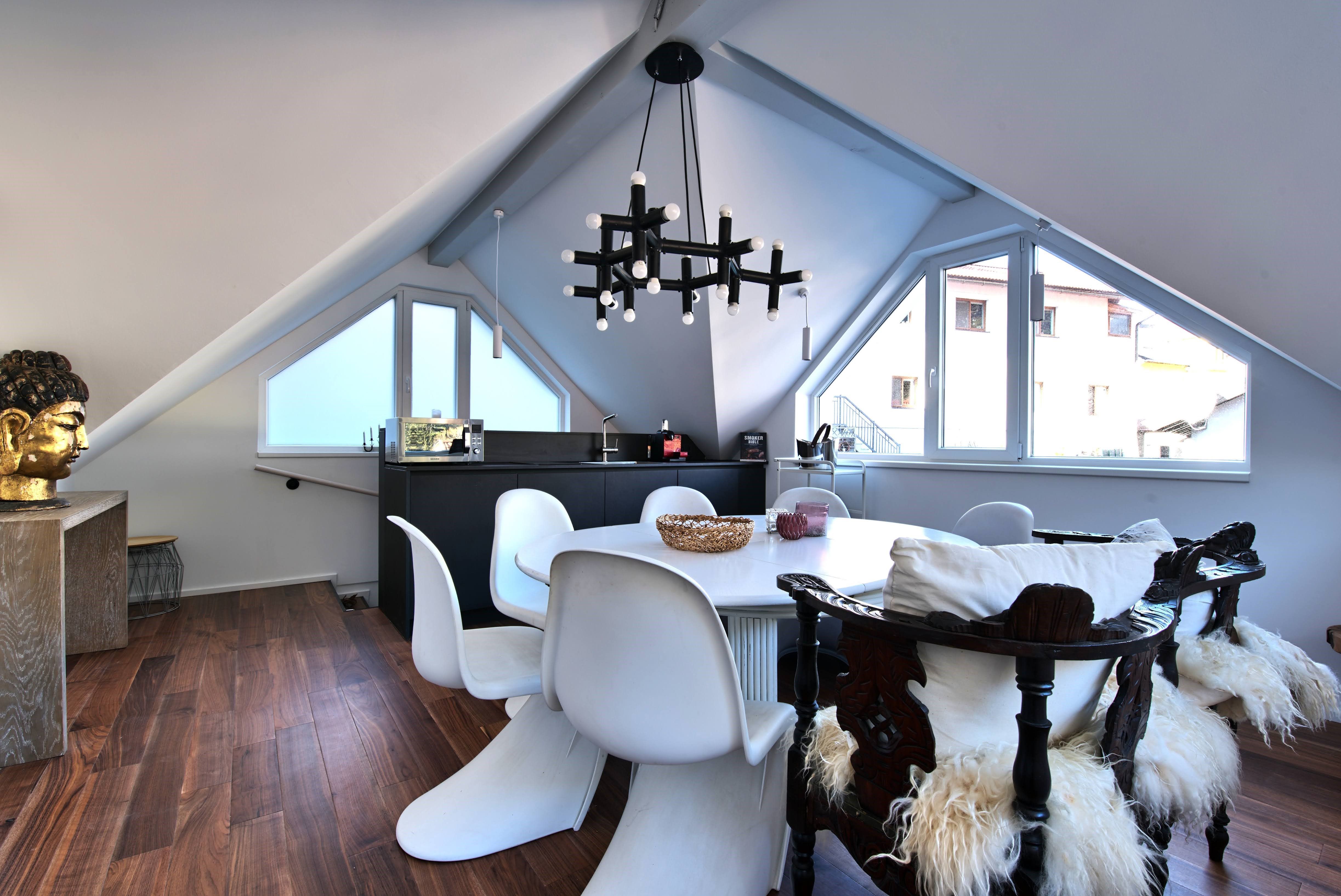 Moderner Essbereich in einem Dachgeschoss mit weißen Stühlen, Holzboden und einem großen Fenster.