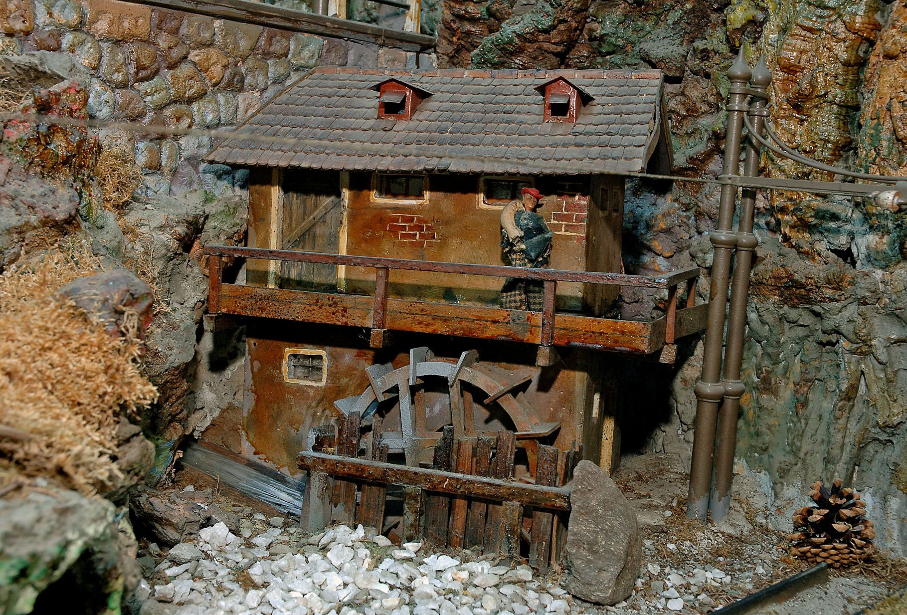 Miniatur-Wassermühle mit Holzrad und kleinem Gebäude in felsiger Umgebung.