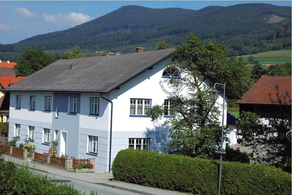 Ein großes, zweistöckiges, weiß-blaues Haus mit Garten und Berglandschaft im Hintergrund.