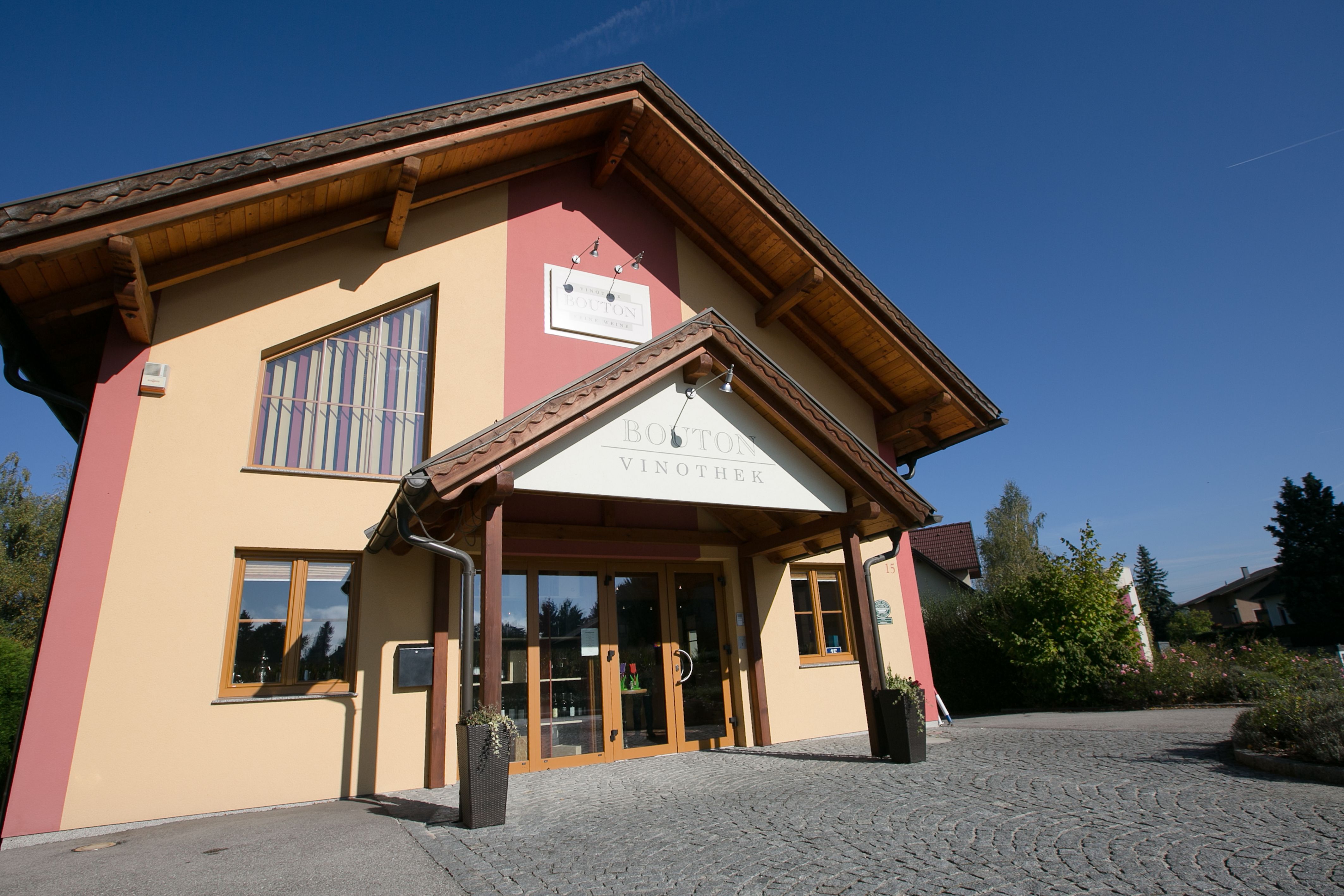 Eingang der Vinothek Bouton mit gelber Fassade und Holzdach.