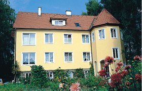 Gelbes Haus mit rotem Dach und Garten im Vordergrund.