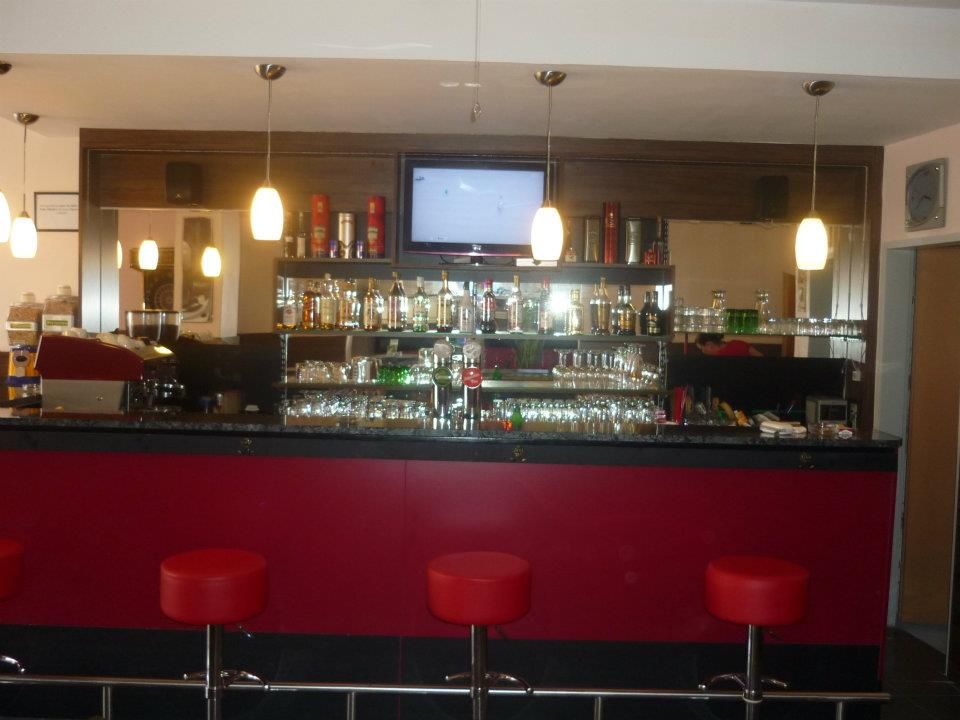 Innenansicht einer Bar mit roten Hockern und beleuchteten Regalen voller Flaschen.