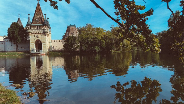 Die majest&auml;tische Franzensburg spiegelt sich im ruhigen Wasser des Teiches wider, umgeben von &uuml;ppigem Gr&uuml;n und sanften H&uuml;geln. Hier, wo Geschichte und Natur harmonisch verschmelzen, l&auml;dt die malerische Kulisse zu einem entspannten Spaziergang ein.