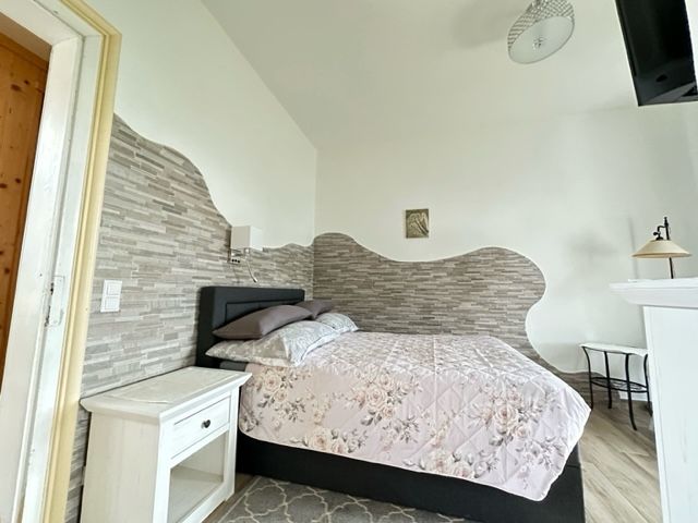 Ein gemütliches Schlafzimmer mit einem Einzelbett, floralem Bettbezug, Nachttisch und dekorativer Wandgestaltung.