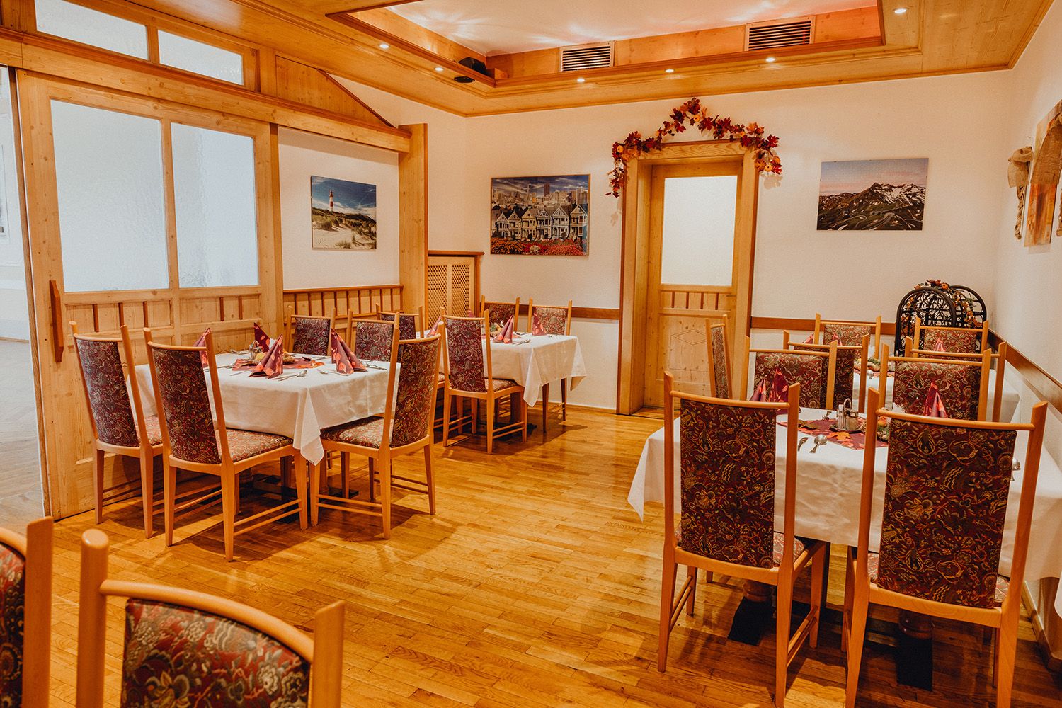 Gemütliche Gaststube mit Holzmöbeln und dekorierten Tischen, umgeben von Bildern an den Wänden.