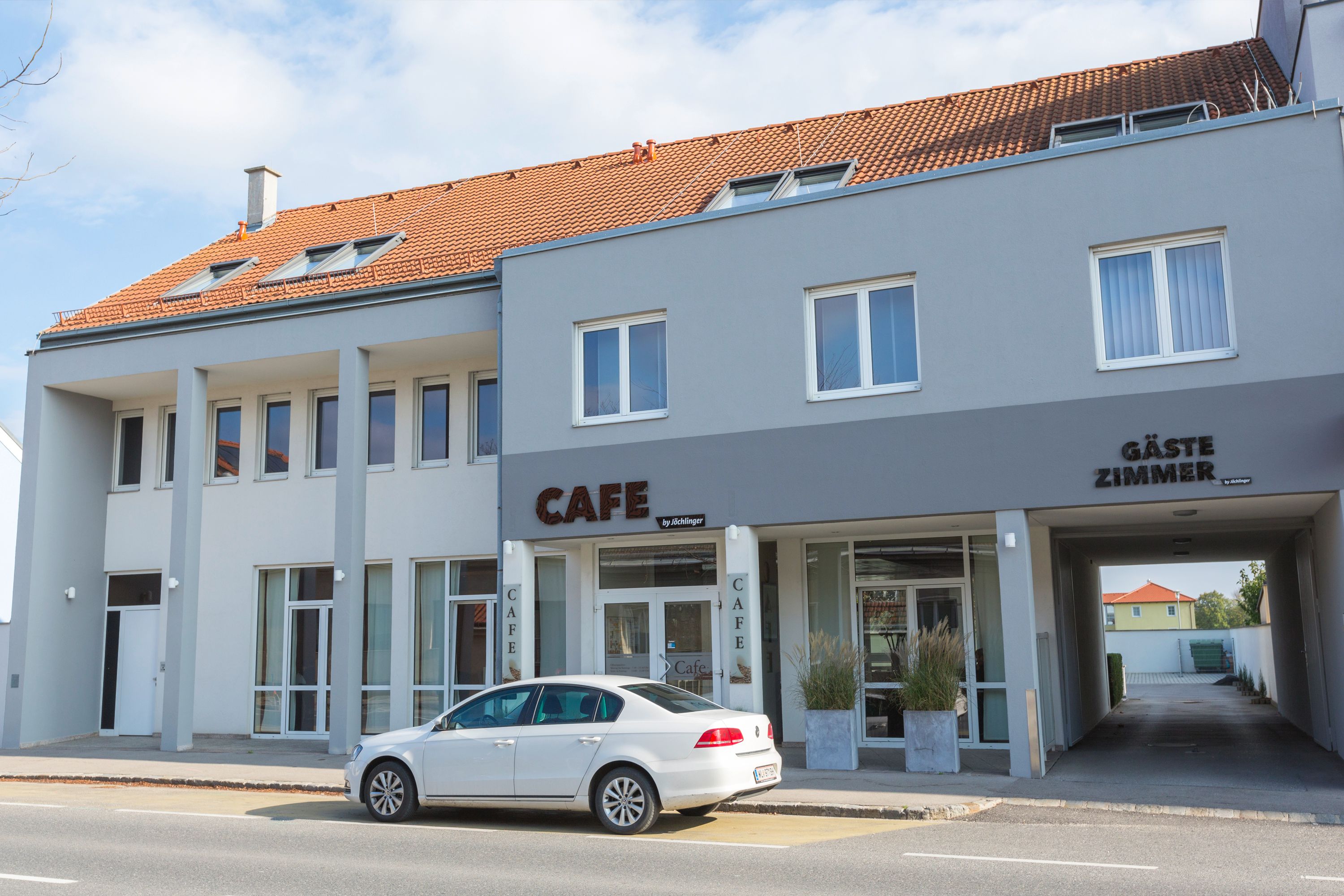 Außenansicht eines grauen Gebäudes mit Café und Gästezimmern.