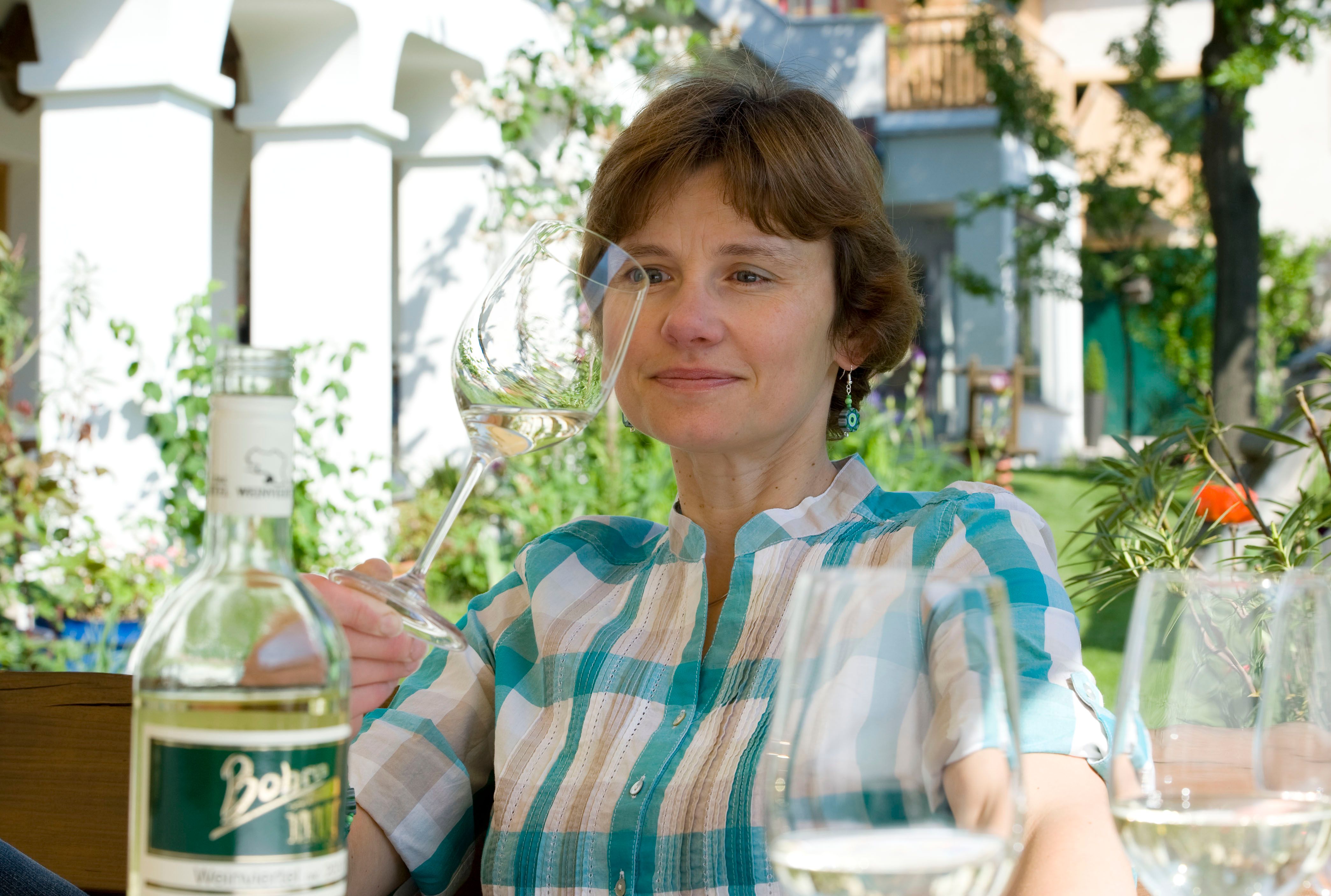 Frau mit Weinglas im Garten, Flasche im Vordergrund.