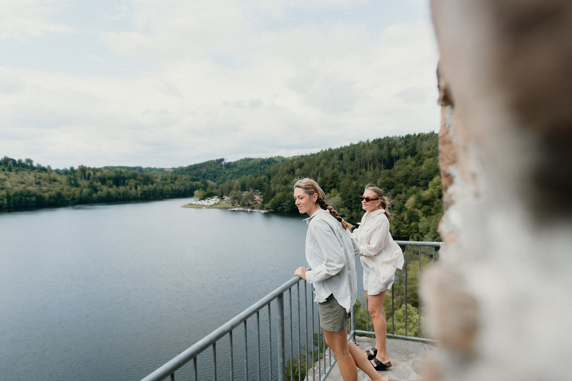 Zwei Personen stehen auf einem Aussichtsbalkon mit Blick auf den Stausee Dobra im Waldviertel. Im Hintergrund sind der See und die bewaldete Landschaft zu sehen.