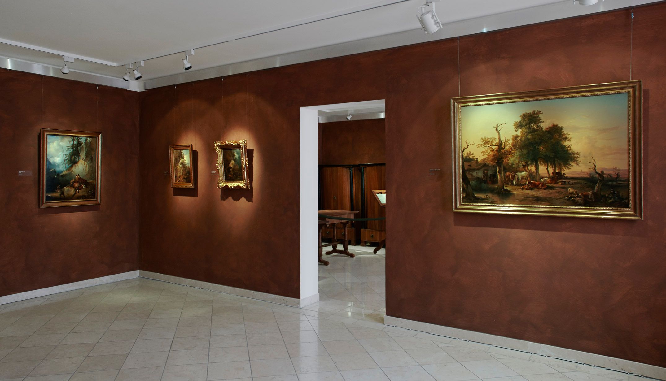 Innenansicht eines Museums mit Gemälden an braunen Wänden.
