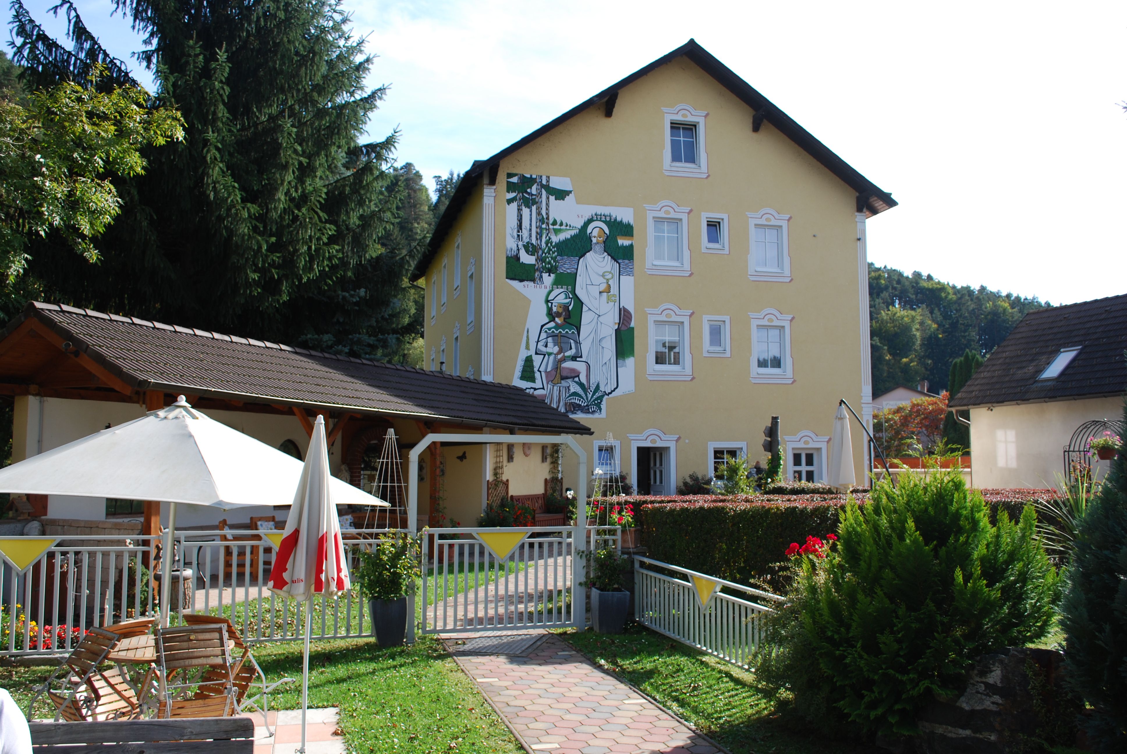 Gelbes Gebäude mit Wandgemälde, Garten mit Sonnenschirm und Sitzbereich.