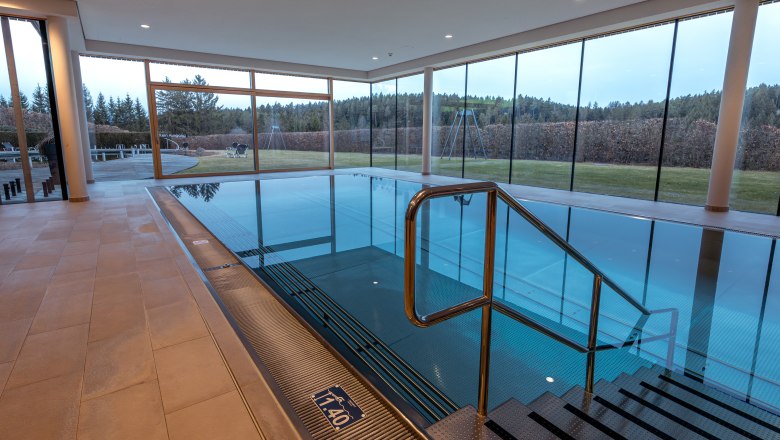 Innenansicht eines modernen Hallenbads mit gro&szlig;en Fenstern und Blick auf die Natur.