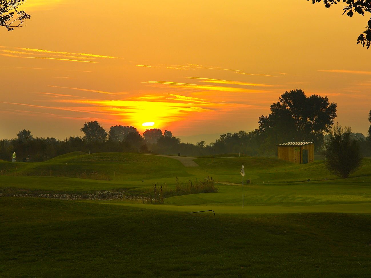 Sonnenuntergang über einem Golfplatz mit Fahne und kleinem Gebäude.