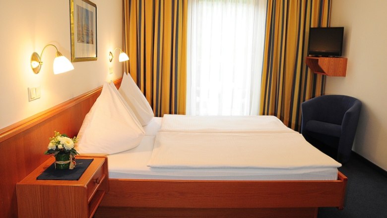 Ein Hotelzimmer mit Doppelbett, blauen Vorh&auml;ngen und einem kleinen Fernseher an der Wand.