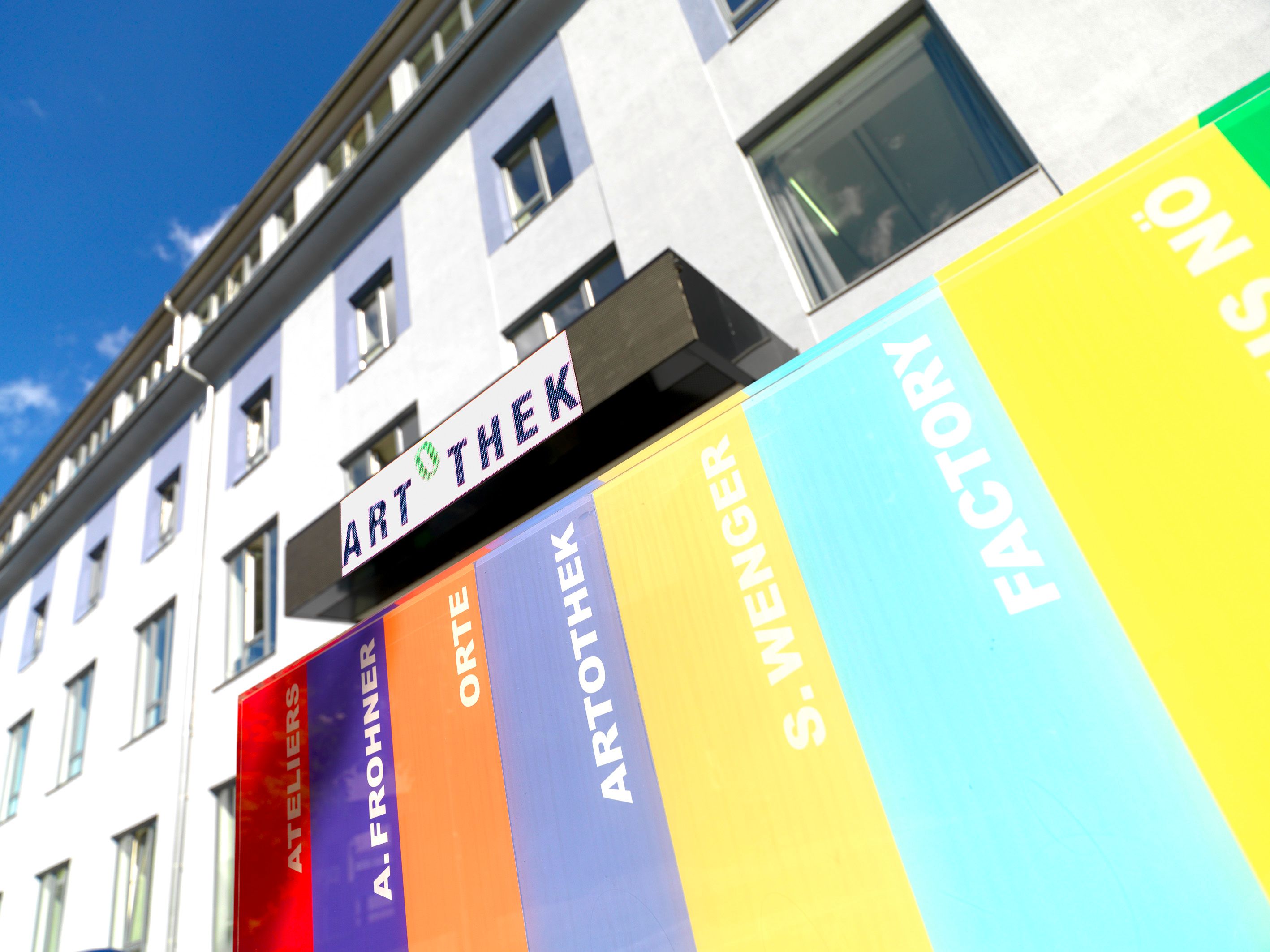 Außenansicht eines Gebäudes mit Artothek-Schild und bunten Streifen.