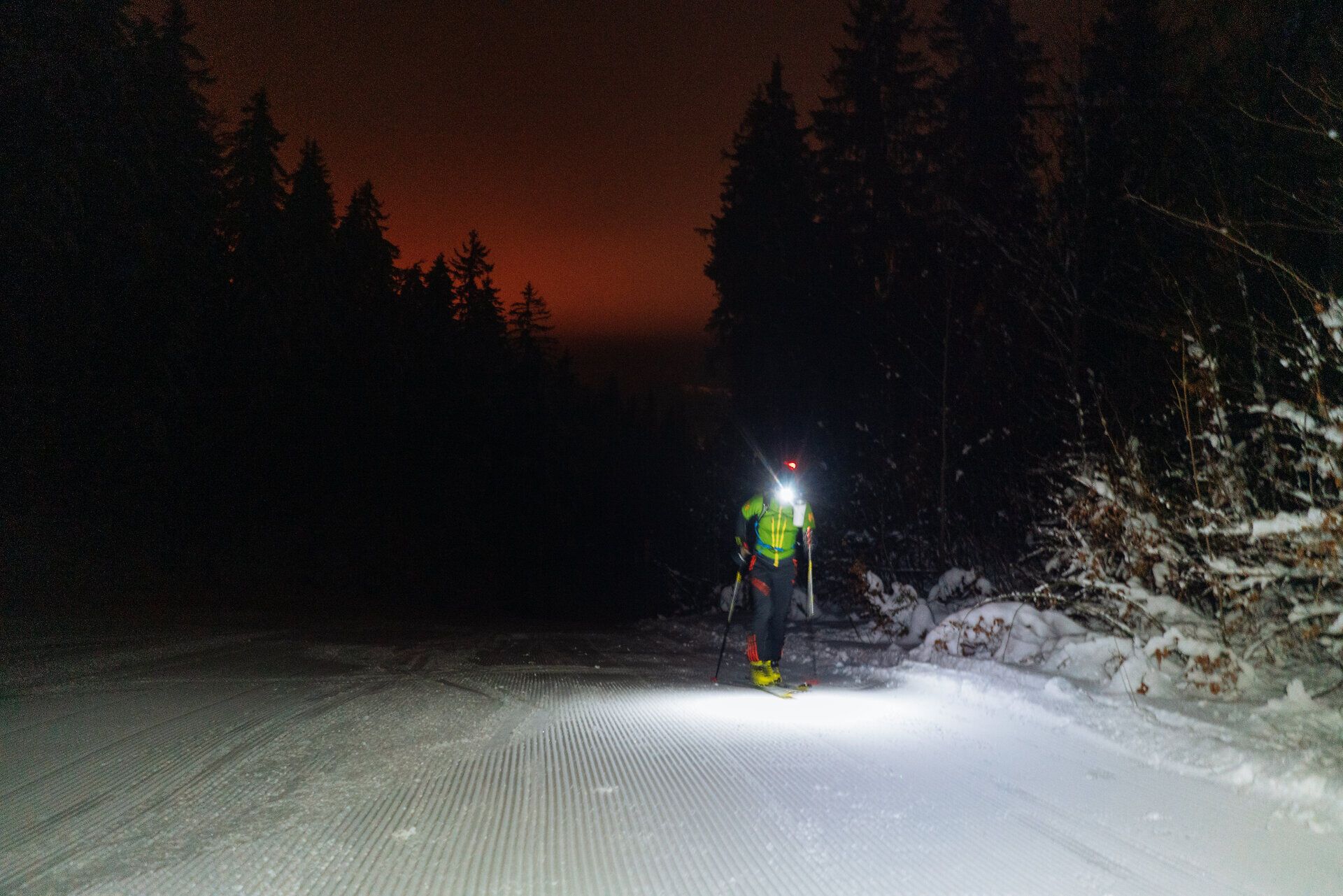 Skitourengeher, der eine Stirnlampe trägt, beim nächtlichen Aufstieg auf einen Berg.