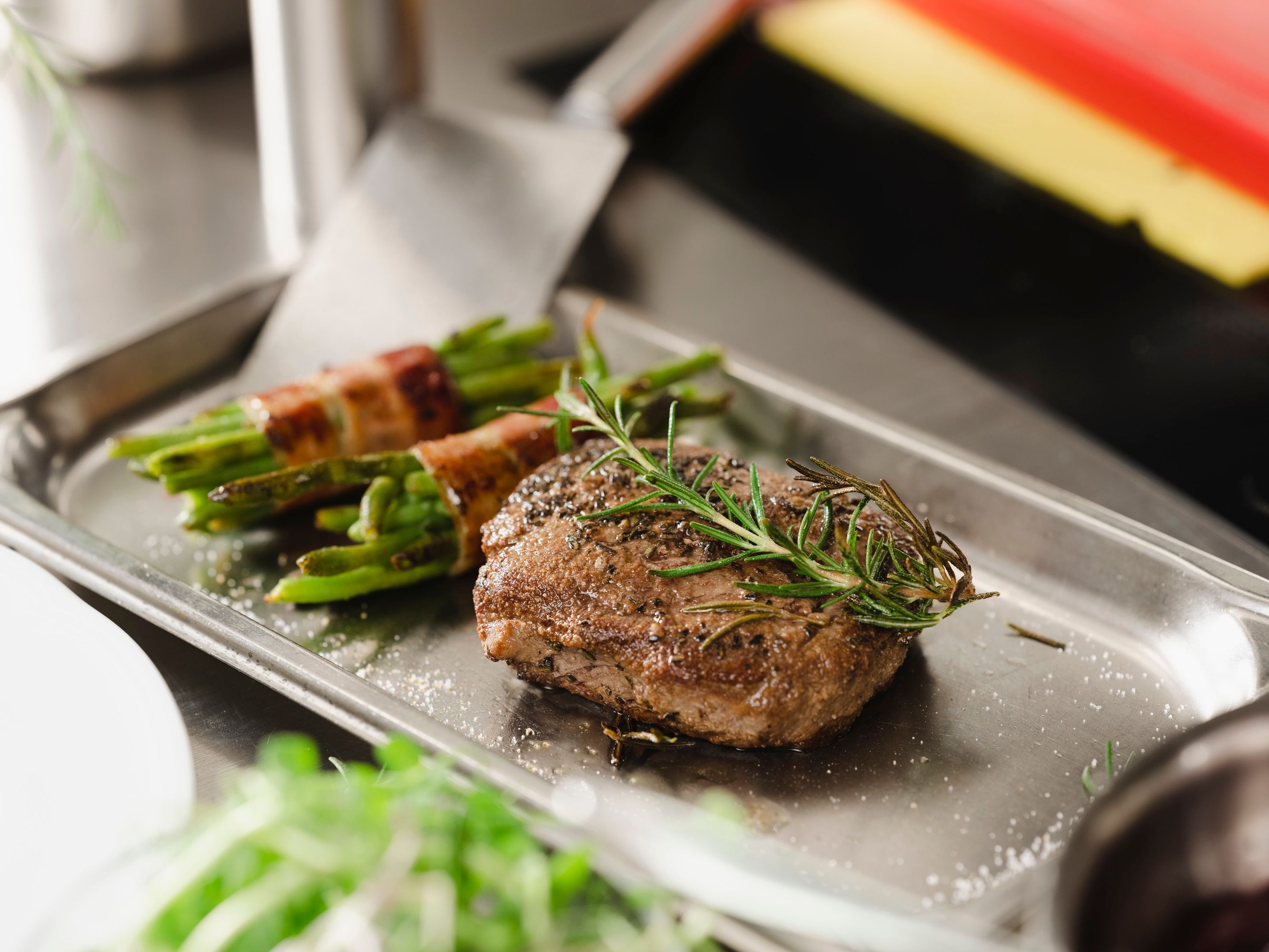 Ein Steak mit Rosmarin und Bohnen im Speckmantel auf einem Metalltablett.