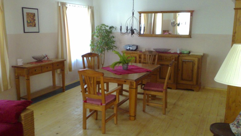 Gemütliches Wohnzimmer mit Holzmöbeln, Esstisch, Stühlen und Pflanzen.